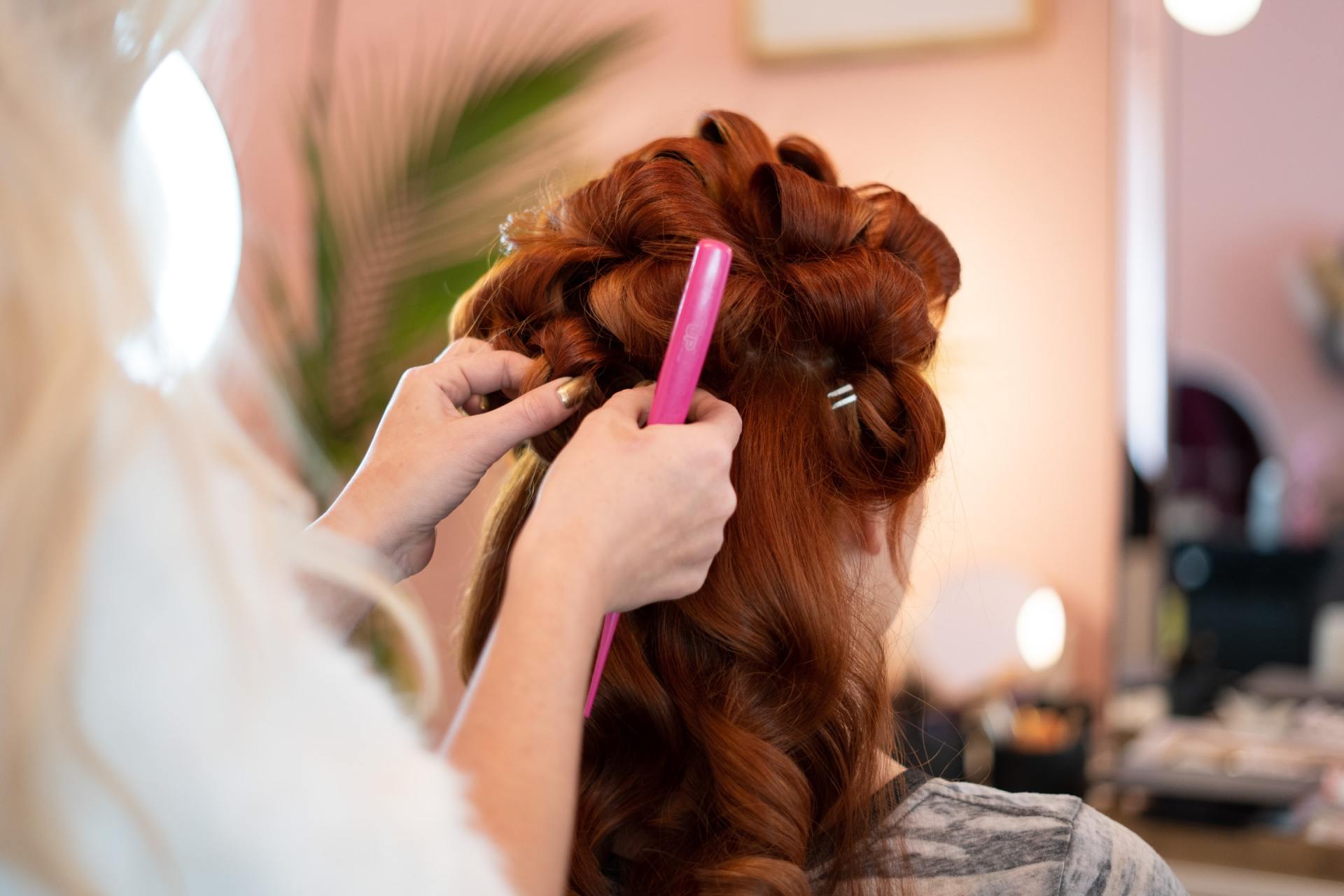 Hairdresser styling reddish-brown hair with a pink comb in a salon.